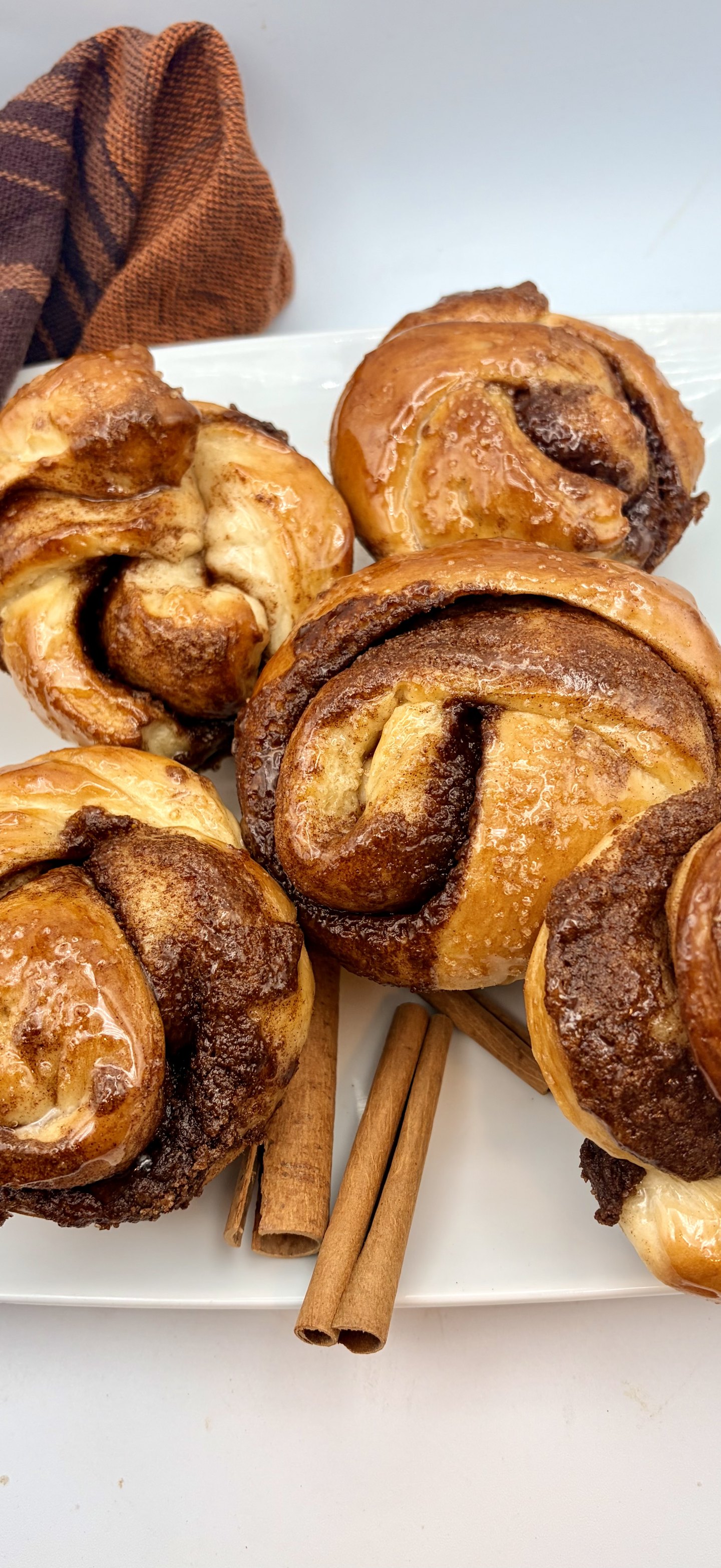 Four glazed cinnamon rolls on a white plate with two cinnamon sticks